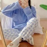 Photo d'une femme qui se prend en photo assise en tailleur dans un pyjama tout doux bleu avec un pantalon à carreau devant un miroir