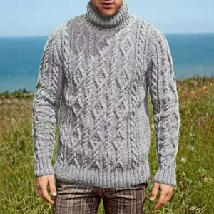Photo d'un homme portant un pull col roulé tricoté à torsade. Derrière lui, de la pelouse et la mer.