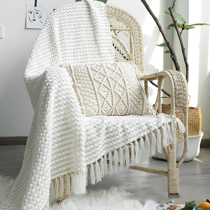 Photo d'une couverture blanche style bohème posée sur une chaise en rotin avec un coussin.