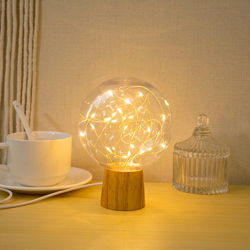 Photo d'une lampe cocooning en boule de cristale avec un support en bois et une guirlande de LED à l'intérieur