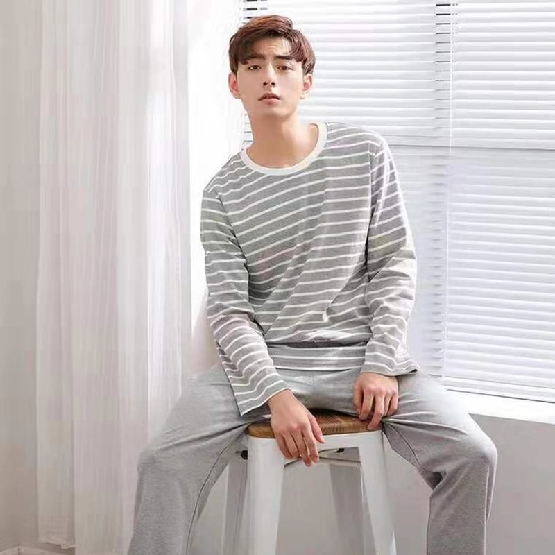 Photo d'un homme assis devant une fenêtre habillé avec un pyjama gris, un bas uni et un haut à rayures.