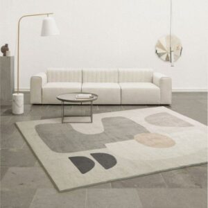 Tapis beige avec un design graphique abstrait posé sur un sol gris devant un canapé blanc dans une pièce minimaliste.
