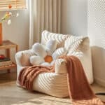mini fauteuil cocooning beige avec un plaid orange dessus et un coussin en forme de fleur
