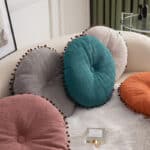 coussins rond colorés avec des pompons, posés sur un canapé blancs avec un plaid fourrure.