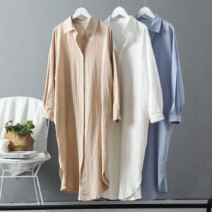 3 robes chemises en coton suspendues par des ceintures devant un mur gris avec une chaise blanche à gauche et un panier en osier dessus.