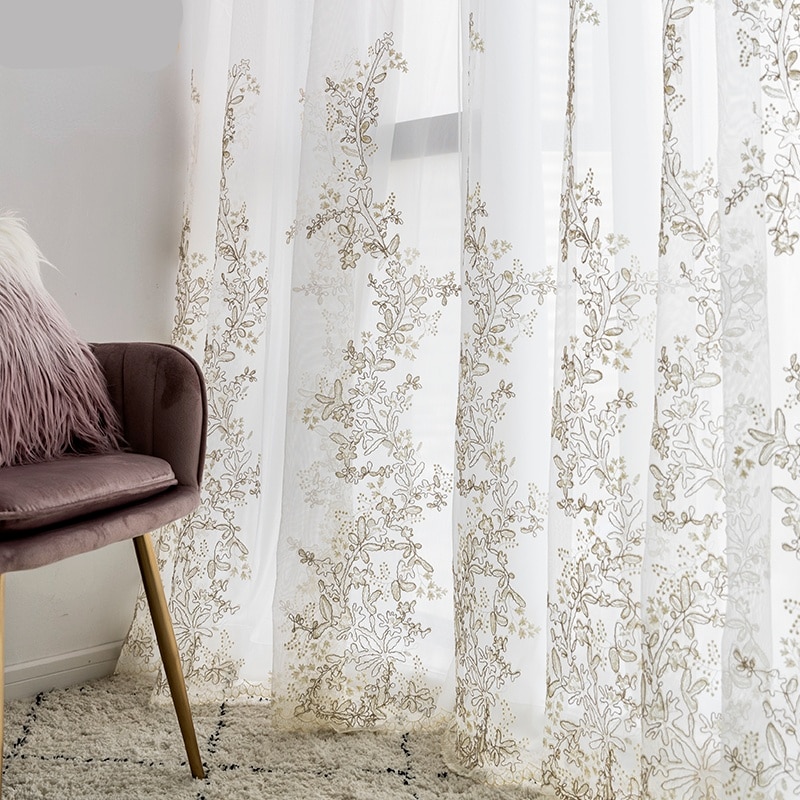 Photo d'un rideau en voilage blanc avec de la dentelle fleurie brodée, beige, devnt une fenêtre avec un siège en velours rose et un pouf à poils longs dessus.