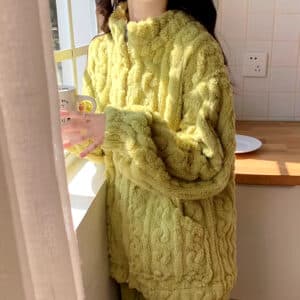 Femme rebord de fenêtre en pyjama épais vert et boit un café