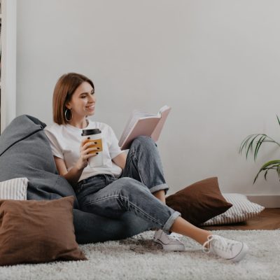 Short-haired girl in white t-shirt with smile reading book while sitting on soft bean bag